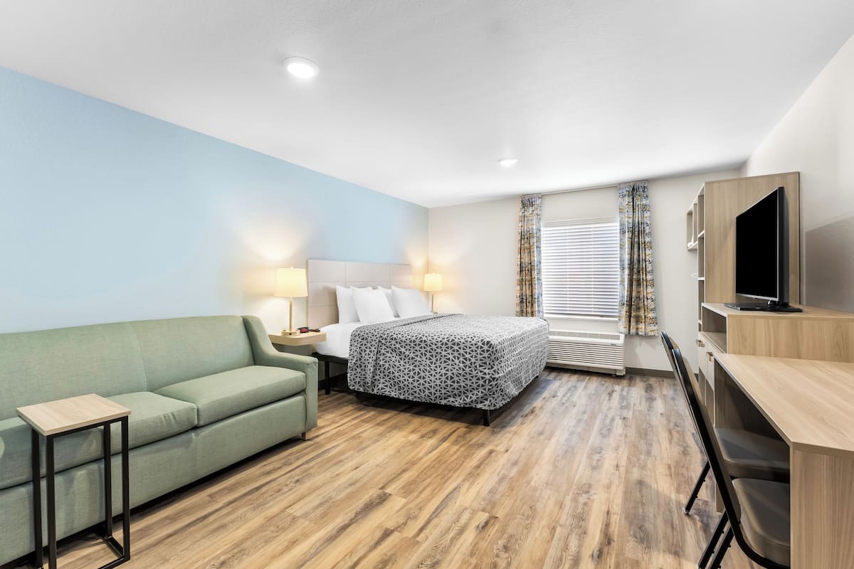 A hotel room with a bed, a sofa, a desk, and a TV.