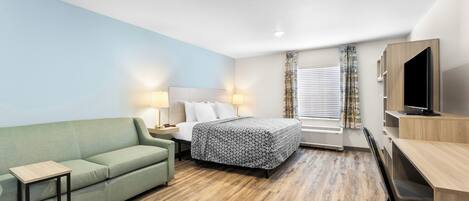 A hotel room with a bed, a sofa, a desk, and a TV.
