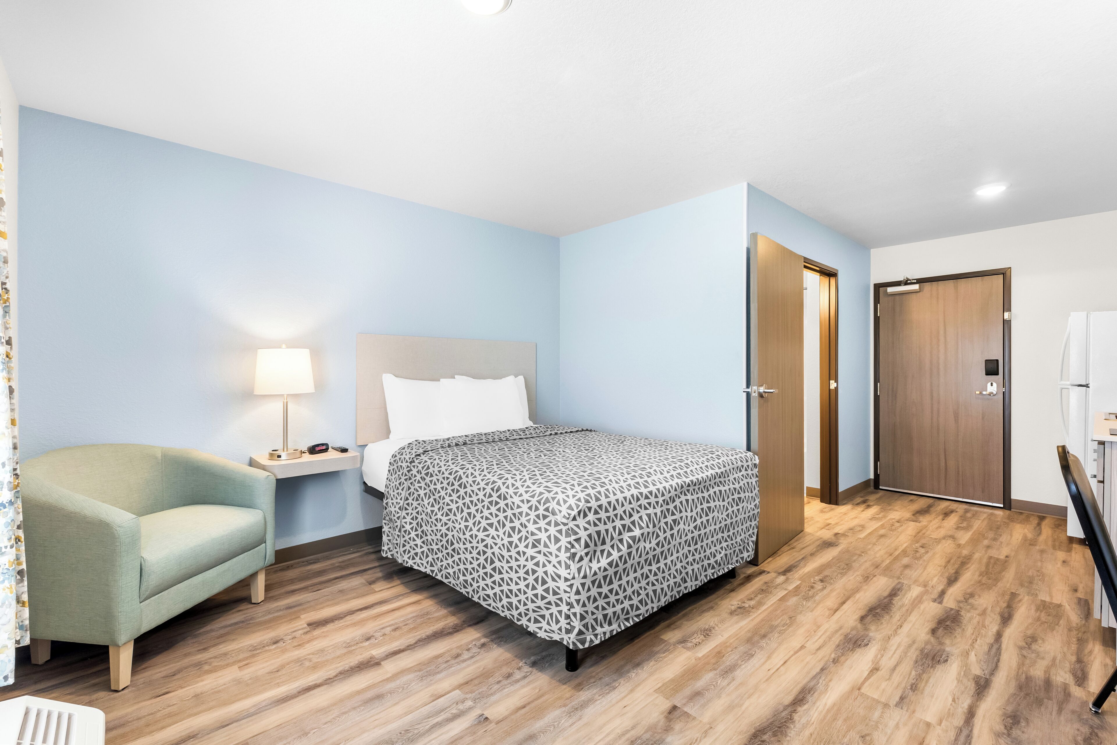 Un dormitorio con cama, mesita de noche, lámpara, una silla y armario.