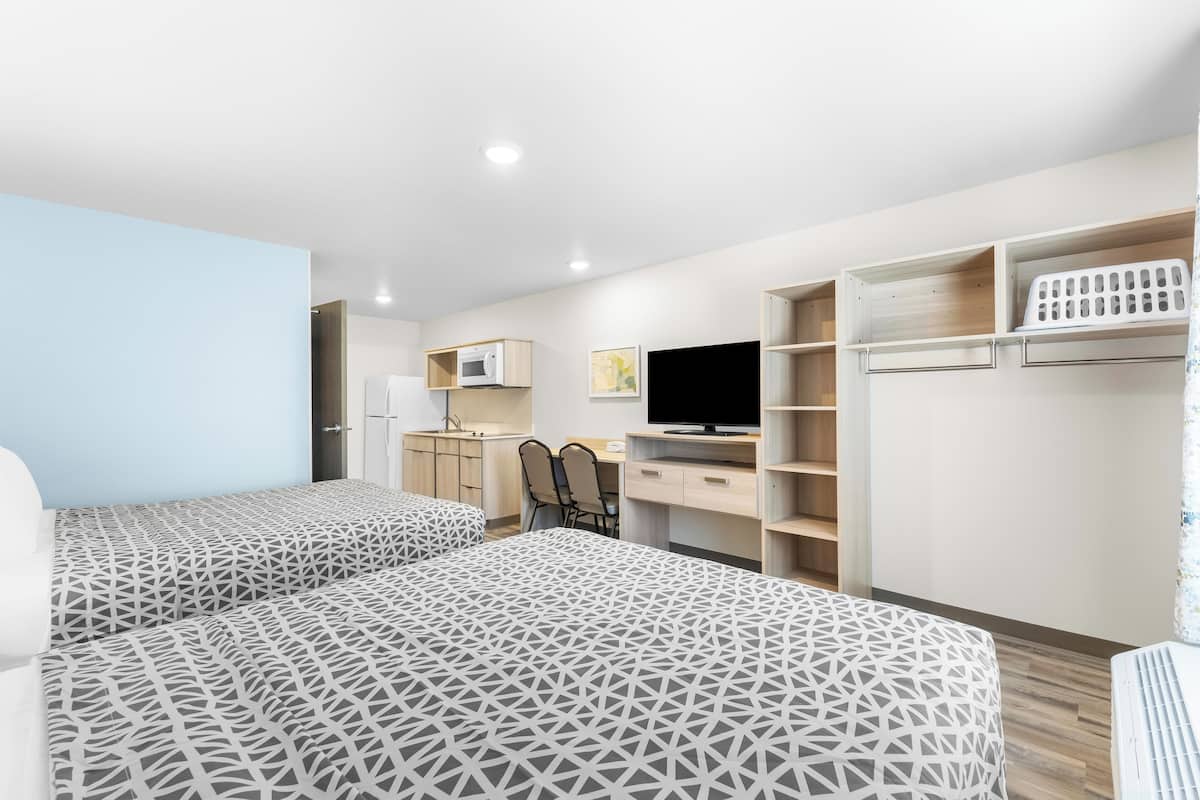 A modern hotel room with two beds, a desk, a TV, and built-in storage.