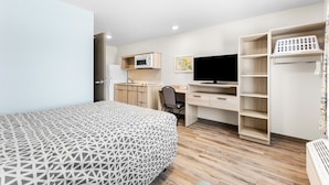 A modern bedroom with a patterned bed, a desk with a computer, a TV, and a wardrobe. - Woodspring Suites Bluffdale Salt Lake City (Bluffdale)
