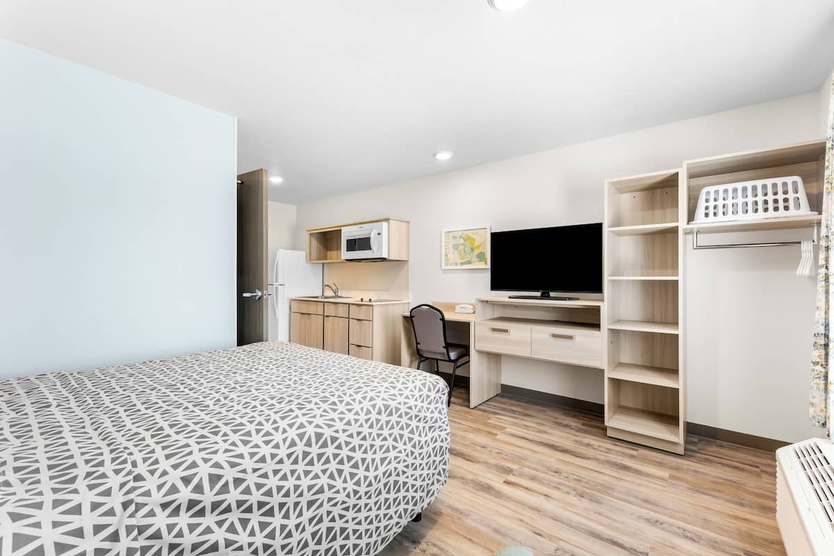 A modern bedroom with a patterned bed, a desk with a computer, a TV, and a wardrobe.