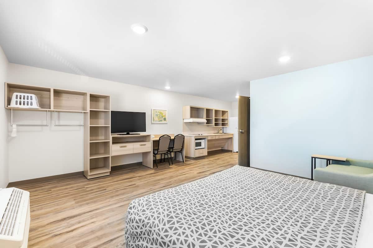 A modern bedroom with a bed, a desk, a chair, and a TV.