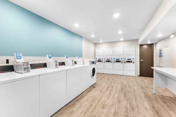 A modern laundry facility with multiple washing machines and dryers, a blue accent wall, and a wooden floor.