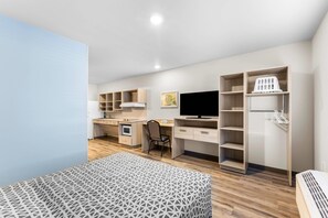 A compact room with a bed, a desk, a television, and built-in shelving.