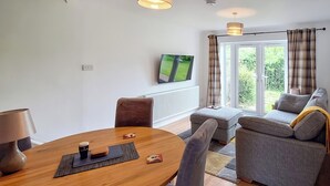Un salon moderne avec une table à manger en bois, un canapé gris et un téléviseur fixé au mur.