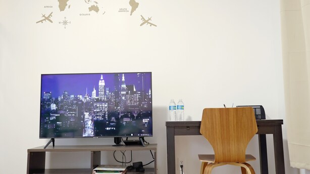 A room with a flat-screen TV displaying a cityscape, a desk with a chair, a world map on the wall, and a water bottle on the desk. - ⭐Cozy 1-Bed⭐Minutes to NYC/PATH (Jersey City)