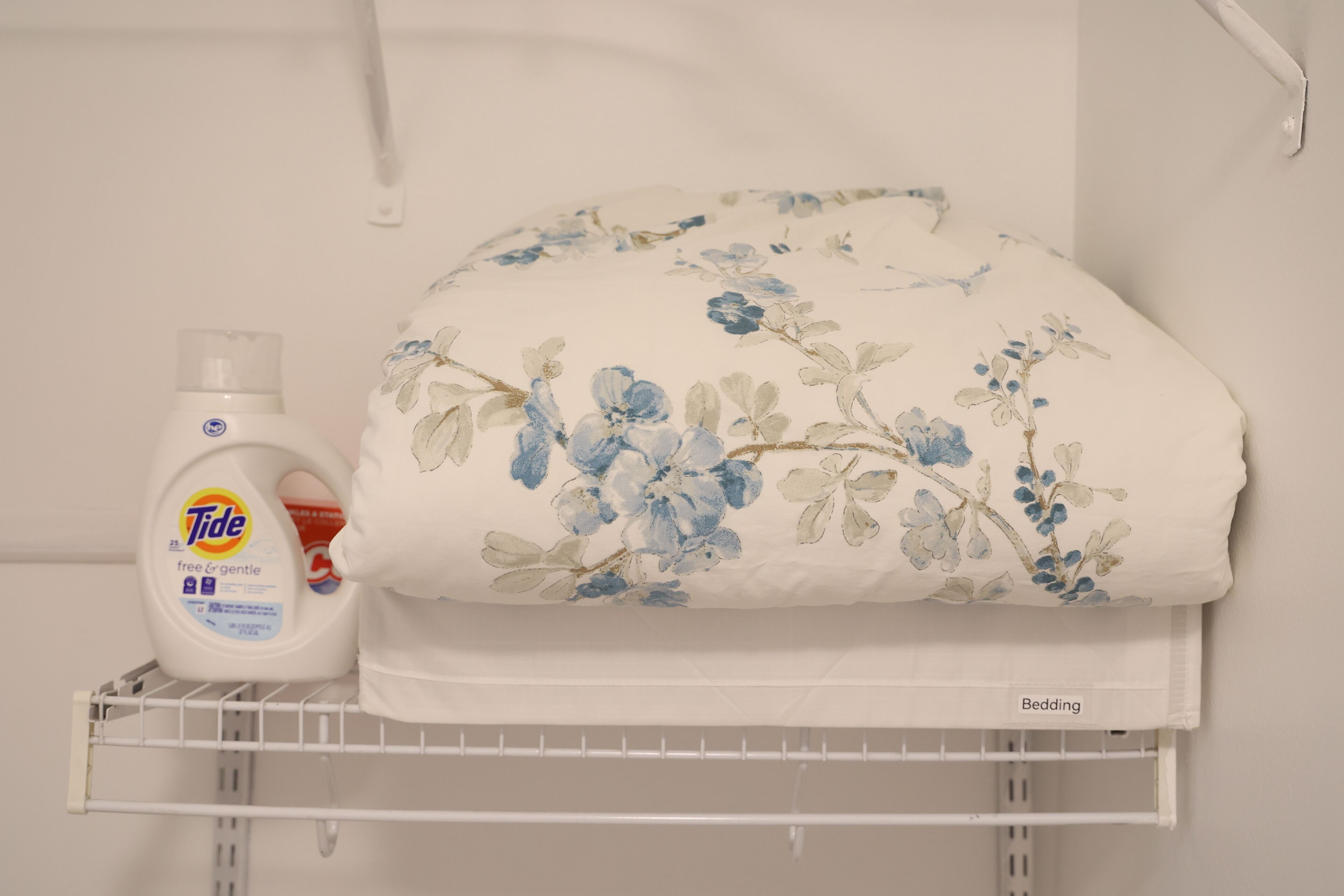 Ein ordentlich eingerichteter Waschbereich mit Tide Waschmittel und einem blumigen Bettwäsche-Set auf einem Regal.