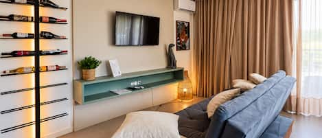 Un salon moderne avec un canapé, un meuble à bouteilles, un téléviseur à écran plat et une grande fenêtre avec des rideaux.