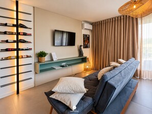 Una sala de estar moderna con un sofá, un mueble bar, un televisor de pantalla plana y un ventanal con cortinas.