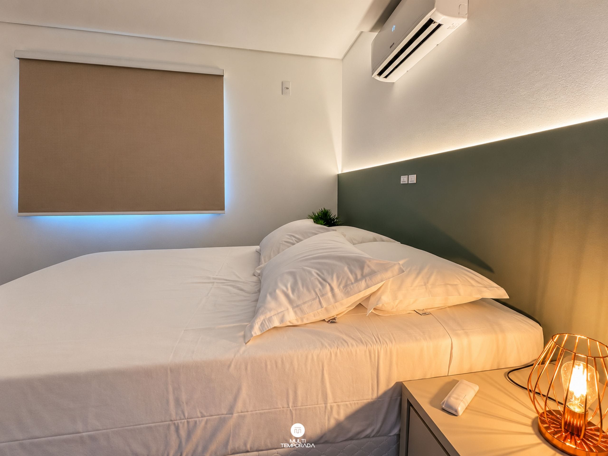 A modern hotel room with a bed, a bedside lamp, and an air conditioning unit.