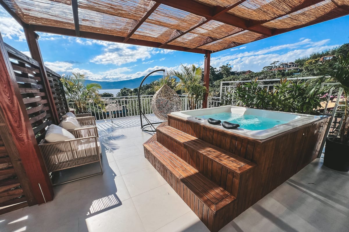 A hot tub with wooden steps, a pergola, and a view of the mountains.
