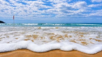 Praia com ondas, uma bandeira e céu claro.