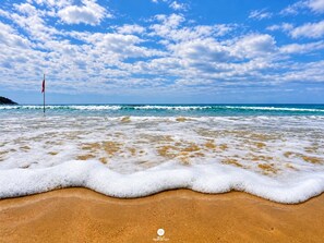 A beach with waves, a flag, and a clear sky. - Villa Verde Bangalô - Garopaba - SC (Garopaba)