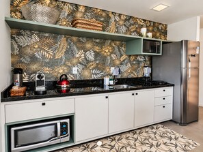 A modern kitchen with a microwave, kettle, and coffee maker on the counter, a refrigerator, and a patterned backsplash. - Villa Verde Bangalô - Garopaba - SC (Garopaba)