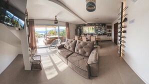 A modern living room with a large sofa, a dining area, and a kitchen. - Villa Verde Bangalô - Garopaba - SC (Garopaba)