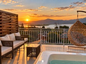A balcony with a sofa, a hanging chair, and a hot tub overlooking a sunset and mountains. - Villa Verde Bangalô - Garopaba - SC (Garopaba)
