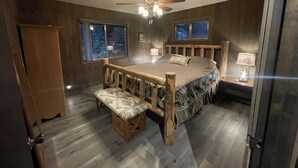 A bedroom with a wooden bed, a bench, a ceiling fan, and two windows.