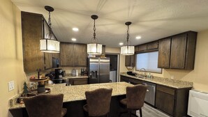 A modern kitchen with granite countertops, dark wooden cabinets, and three bar stools.