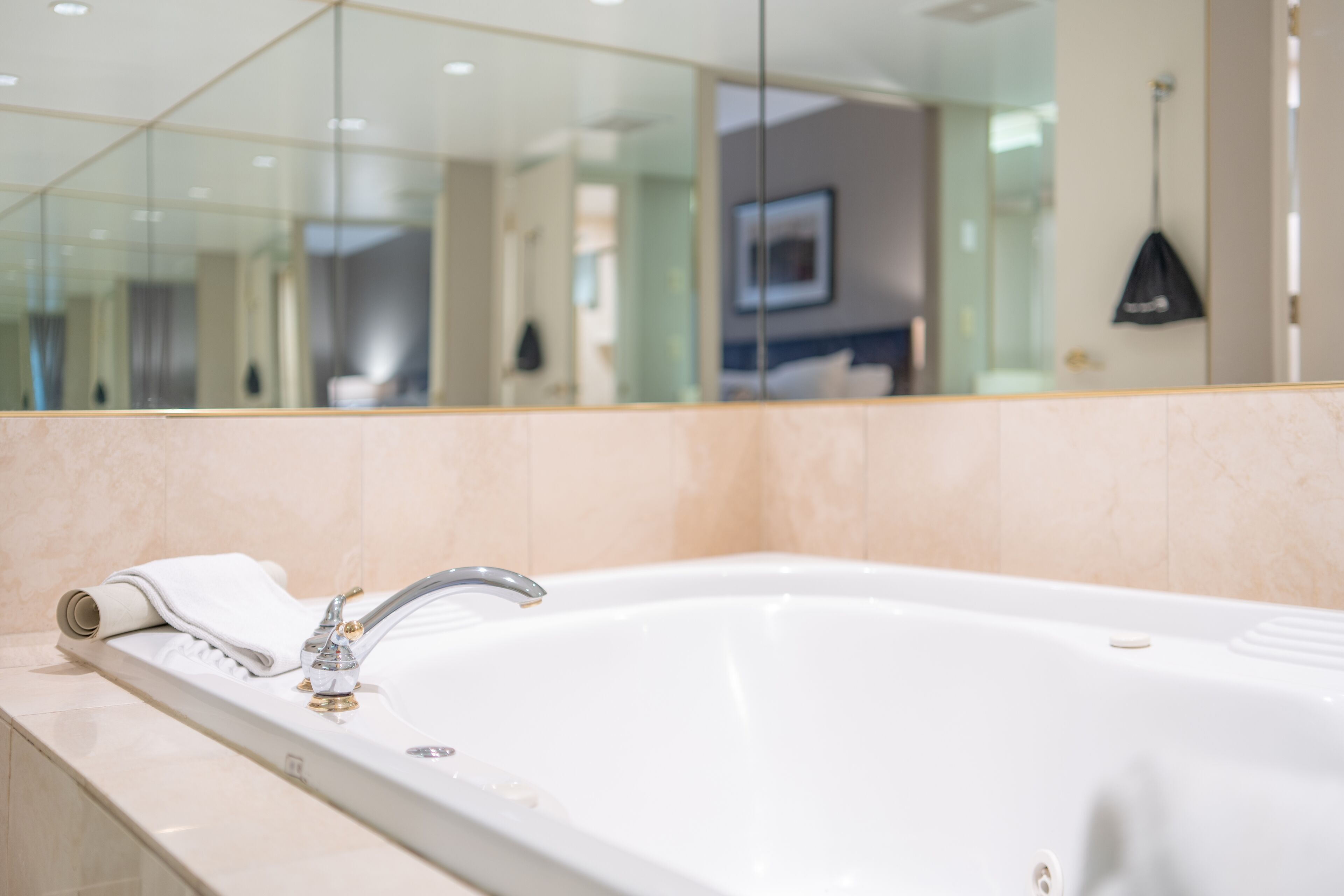 A modern bathroom with a large white bathtub, a mirror, and a towel on the edge.