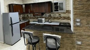 Una cocina moderna con armarios de madera oscura, un refrigerador de acero inoxidable, un microondas y una estufa a gas. Hay dos taburetes de bar y una pequeña isla con un lavamanos.
