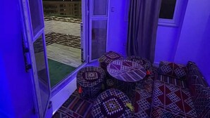 Una habitación con piso estampado, una mesa con taburetes y vista al exterior de noche.