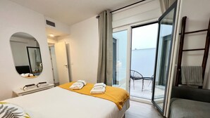 Habitación de hotel con cama, mesita de noche con toallas, un espejo y vistas al balcón.