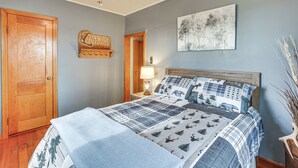 Et soveværelse med en seng, en trædør, et natbord med lampe, en loftsvifte og et billede på væggen.