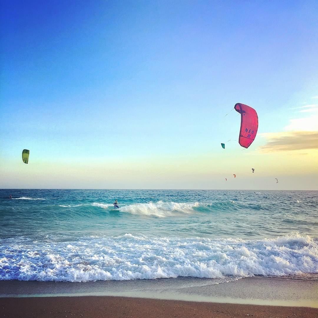 A beach with clear skies and multiple kites flying.