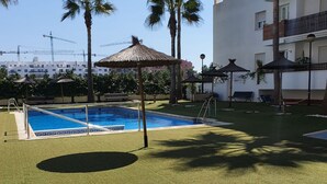 A swimming pool area with two pools, palm trees, and a thatched umbrella. - PUSHE Playa Granada Beach & Golf 17 (Motril)