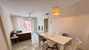 A modern living room with a sofa, a dining table with chairs, a ceiling fan, and a hanging light fixture. - PUSHE Playa Granada Beach & Golf 17 (Motril)