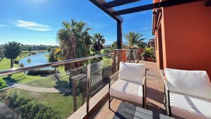 Un balcon doté d’une balustrade en verre, offrant une vue sur un terrain de golf et un plan d’eau.