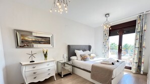 Une chambre à coucher moderne avec un grand lit, une commode, une table de chevet et un tableau au mur.