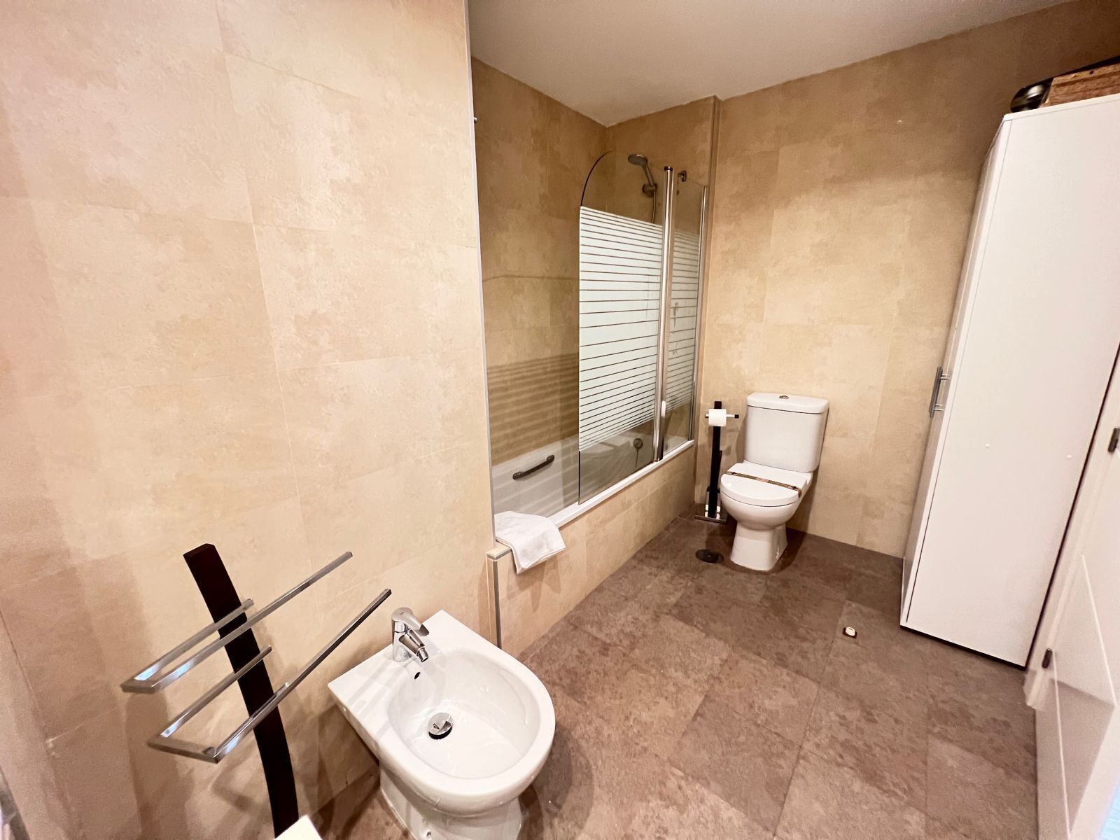A bathroom with a bidet, toilet, and a glass-enclosed shower.