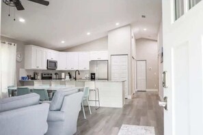 Una cocina moderna con armarios blancos, una isla central y una zona de comedor con un sofá gris.