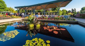 A serene outdoor area with a reflective pond, a covered seating area, and a variety of colorful flowers. - ᨒFIREHAUSᨒHotTubᨒCinemaᨒBBQᨒBadmintonᨒGames (Arvada)