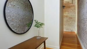 Un pasillo con pared de ladrillo, un espejo redondo, un banco de madera y una planta en maceta.
