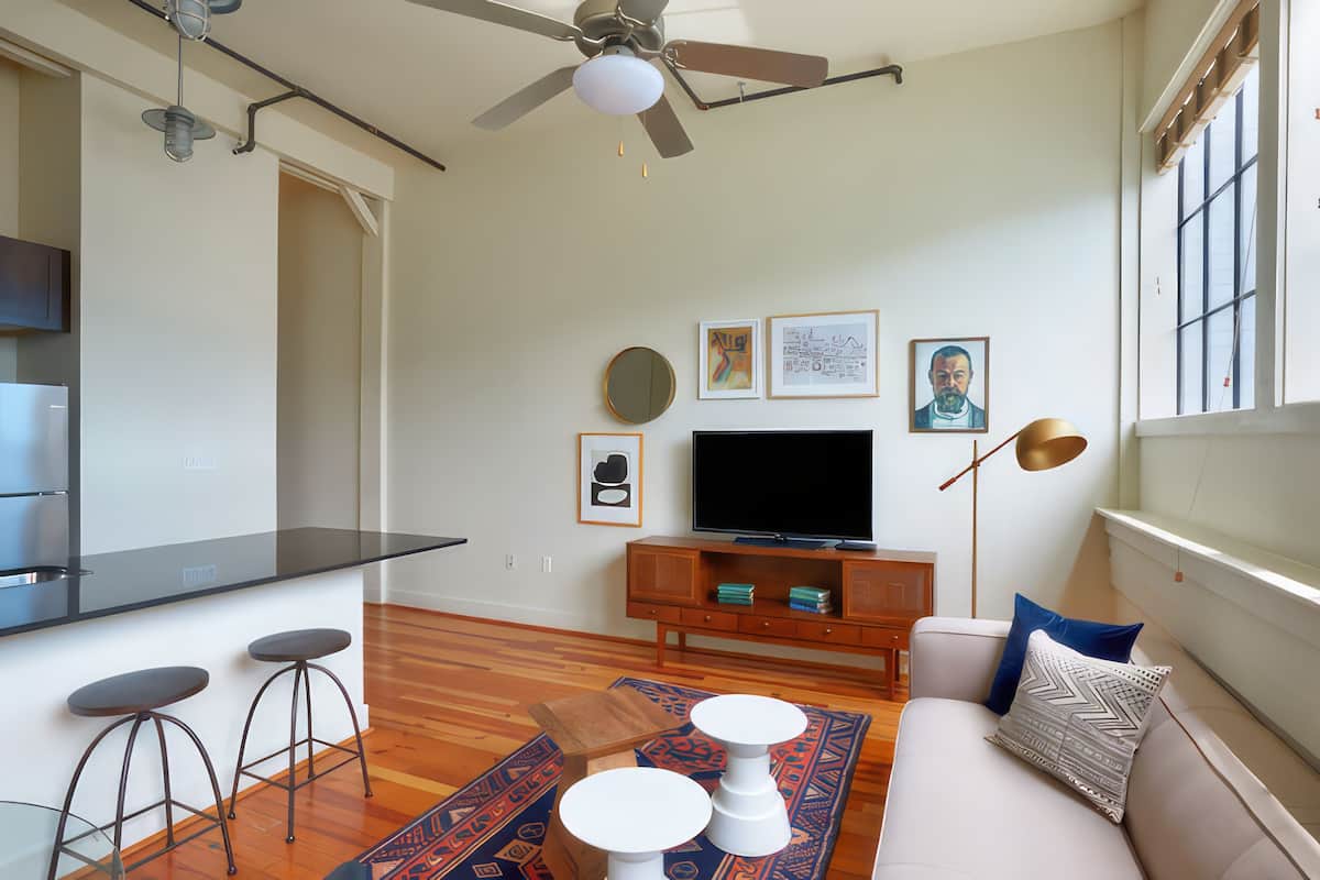 Un salon moderne doté d’un téléviseur à écran plat, de planchers en bois, d’un ventilateur de plafond et d’un canapé agrémenté de coussins décoratifs.
