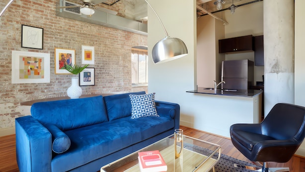 Una sala moderna con un sofá azul, una silla negra y una mesa de centro de vidrio.