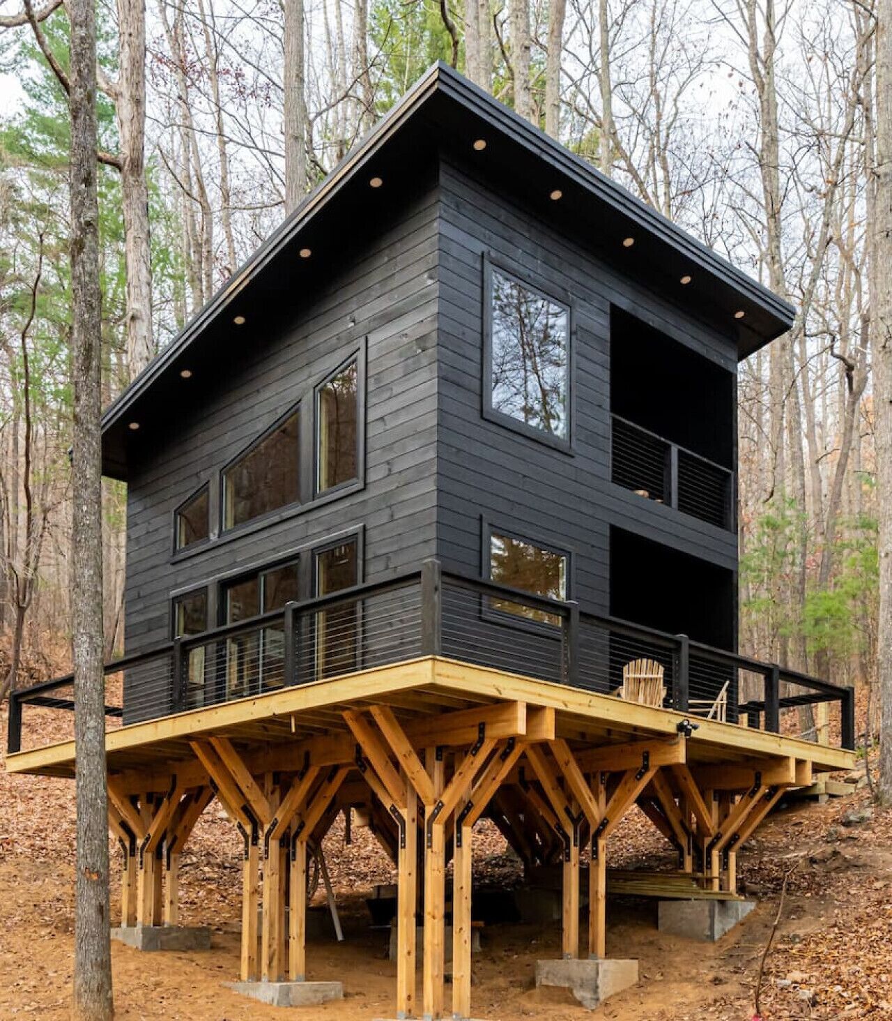 A two-story cabin with a deck, surrounded by trees.