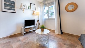 A modern living room with a TV, a round table with a plant, a framed picture, and a round mirror on the wall.