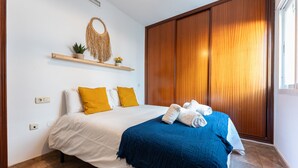 A bedroom with a bed, a wooden wardrobe, a shelf with plants, and a macrame wall hanging.