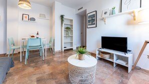 A modern living room with a TV, white shelves, and a dining area with chairs.