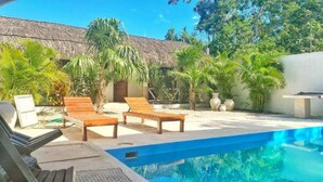 A pool area with lounge chairs and a thatched-roof building. - Casa Macay Tulum (Tulum)