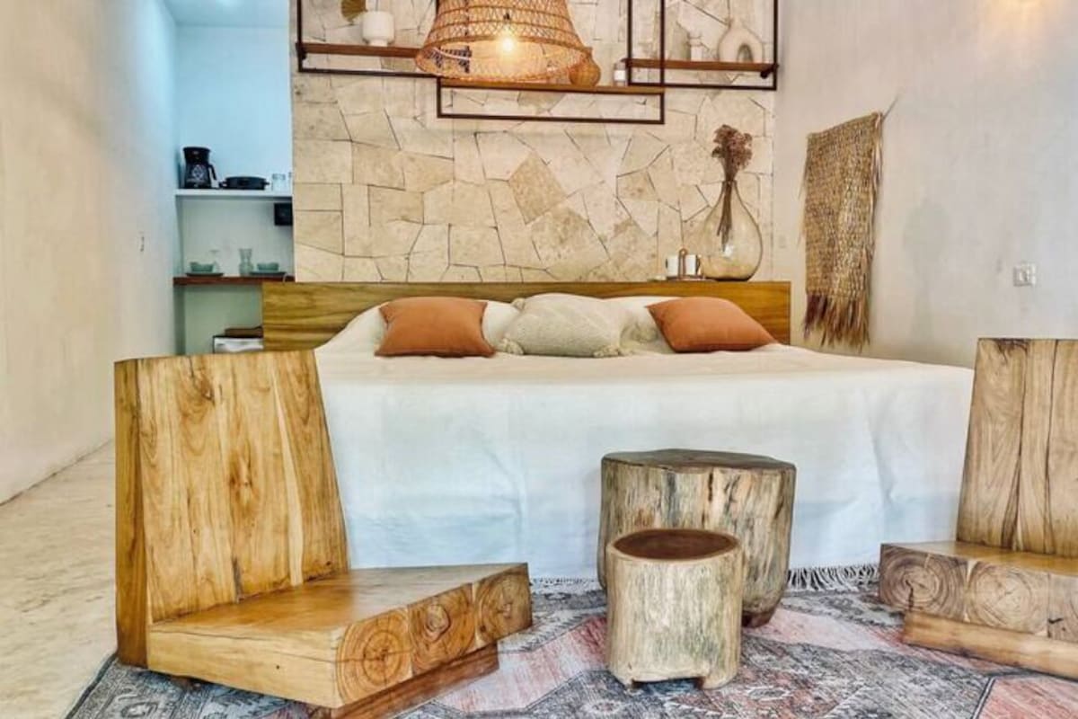 A bedroom with a bed, wooden side tables, a stone wall, and a hanging light fixture.