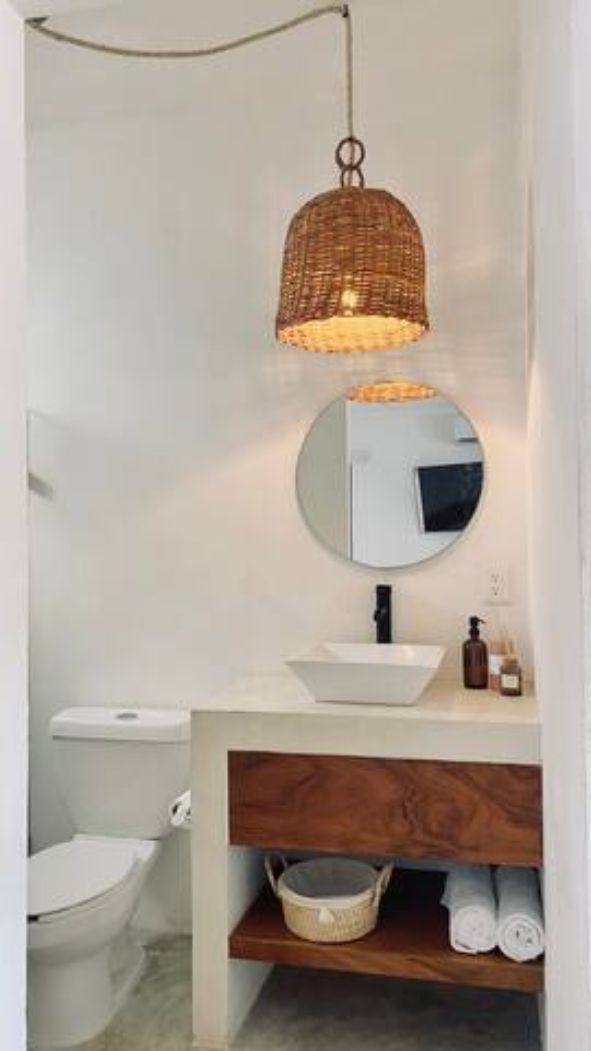 A modern bathroom with a round mirror, a white sink, and a hanging light fixture.