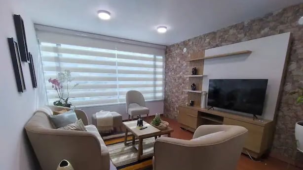 Ett modernt vardagsrum med en soffa, fåtöljer, ett soffbord och en tv.