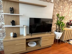 Een moderne woonkamer met een flatscreen televisie bevestigd aan een houten wandmeubel, een potplant en een decoratief beeldhouwwerk.