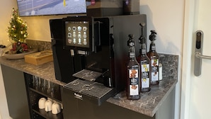 Una máquina de café con pantalla digital, un pequeño árbol de Navidad y botellas de coñac francés sobre una encimera de mármol.