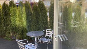 Un patio con sillas y una mesa de metal, rodeado de follaje y vistas a un cuerpo de agua.
